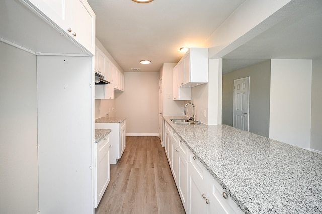 6514 Kentwick Dr, Houston, TX 77084 - kitchen featuring light wood-style flooring, white cabinetry, light stone counters, under cabinet range hood, and a sink