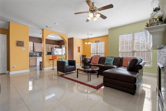 living area with arched walkways, visible vents, ceiling fan with notable chandelier, and baseboards