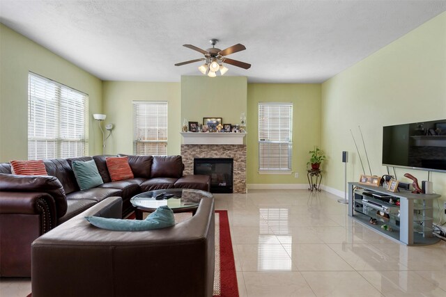 living room featuring a ceiling fan, a textured ceiling, a fireplace, light tile patterned floors, and baseboards