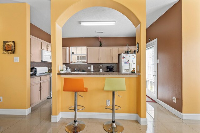 kitchen with arched walkways, backsplash, white appliances, and dark countertops