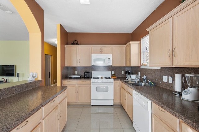 kitchen with a sink, white appliances, dark countertops, and light brown cabinetry