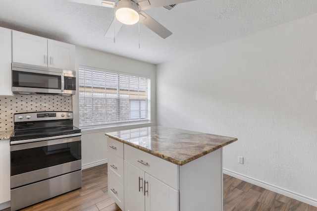 kitchen featuring decorative backsplash, wood finished floors, white cabinets, stainless steel appliances, and a ceiling fan