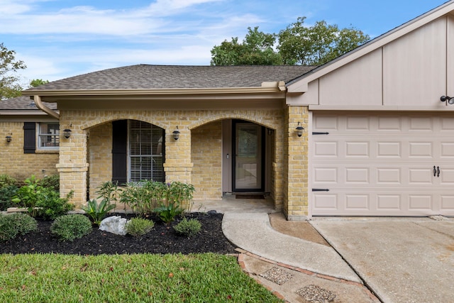 view of exterior entry featuring brick siding, an attached garage, concrete driveway, and roof with shingles