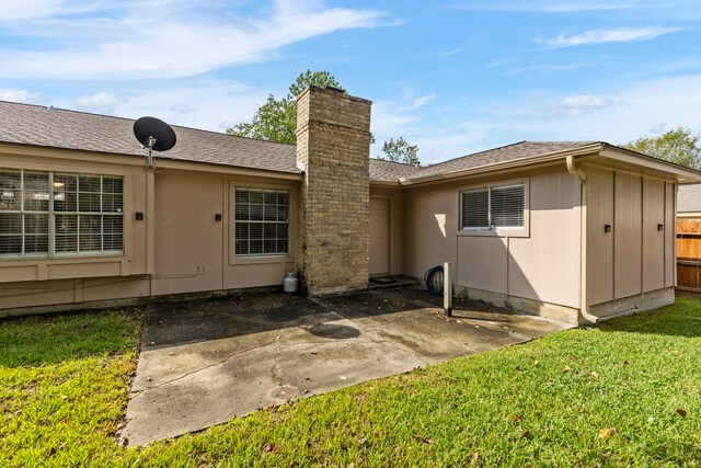 rear view of house with a patio, a yard, roof with shingles, and a chimney