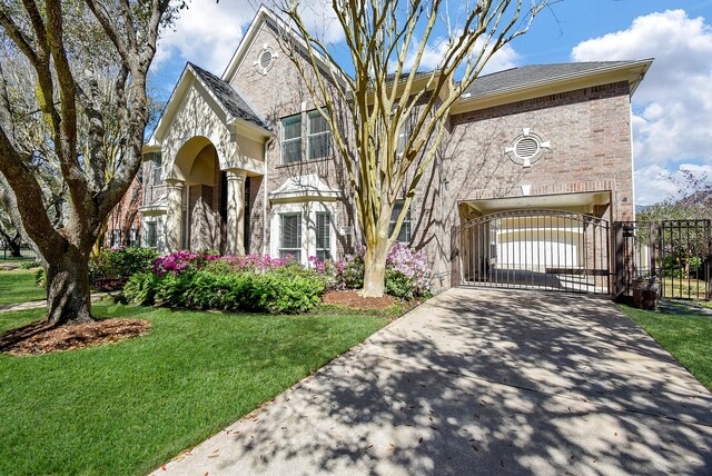 view of front of house with a front lawn, a gate, brick siding, and driveway