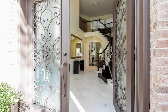 foyer entrance with stone tile floors, stairway, arched walkways, a high ceiling, and brick wall