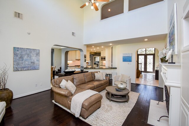 living room with visible vents, a ceiling fan, arched walkways, baseboards, and dark wood-style flooring