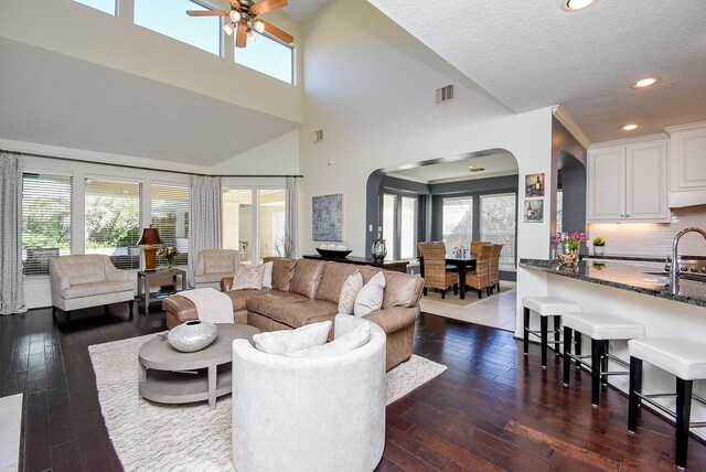 living area with dark wood finished floors, visible vents, arched walkways, and a healthy amount of sunlight