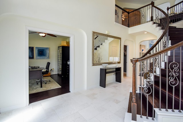 entrance foyer with ceiling fan, arched walkways, baseboards, a towering ceiling, and stairs