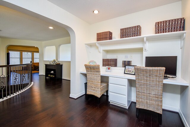 office space featuring baseboards, recessed lighting, arched walkways, built in desk, and wood-type flooring