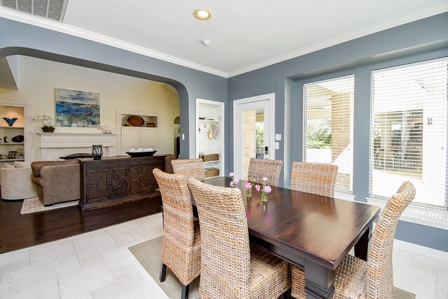 dining room featuring visible vents, baseboards, a fireplace, arched walkways, and crown molding