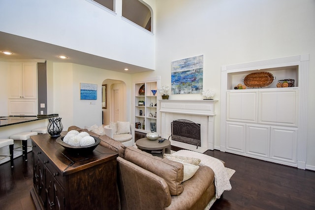living area featuring built in shelves, recessed lighting, arched walkways, a fireplace, and dark wood-style flooring