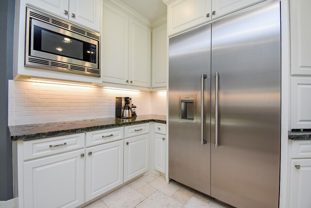 kitchen with decorative backsplash, white cabinetry, built in appliances, and stone tile flooring