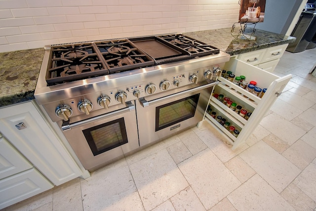 details with double oven range, tasteful backsplash, white cabinets, and dark stone counters