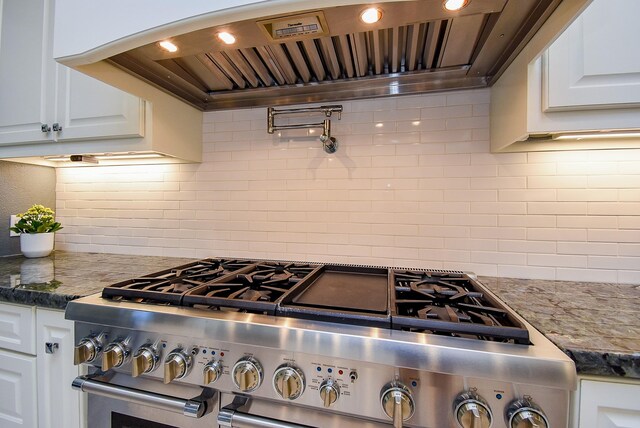 kitchen with high end stainless steel range oven, range hood, decorative backsplash, and white cabinets