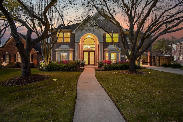 view of front of house featuring french doors, driveway, brick siding, and a front lawn