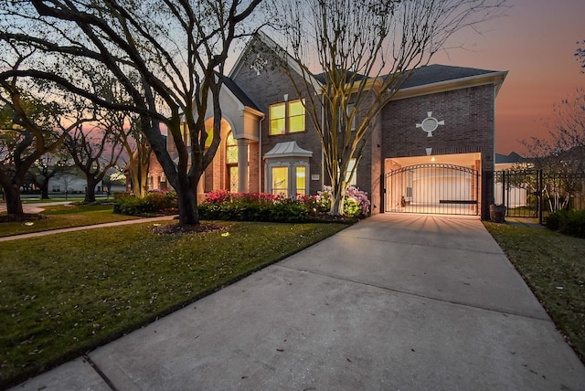 view of front facade with a yard, brick siding, concrete driveway, and a gate