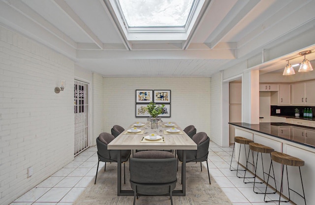 dining room with light tile patterned floors, beamed ceiling, brick wall, and a skylight