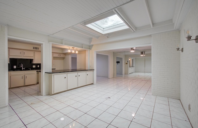 kitchen with visible vents, dark countertops, a skylight, brick wall, and light tile patterned floors