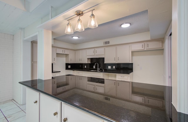 kitchen with a sink, visible vents, decorative backsplash, and dark stone countertops