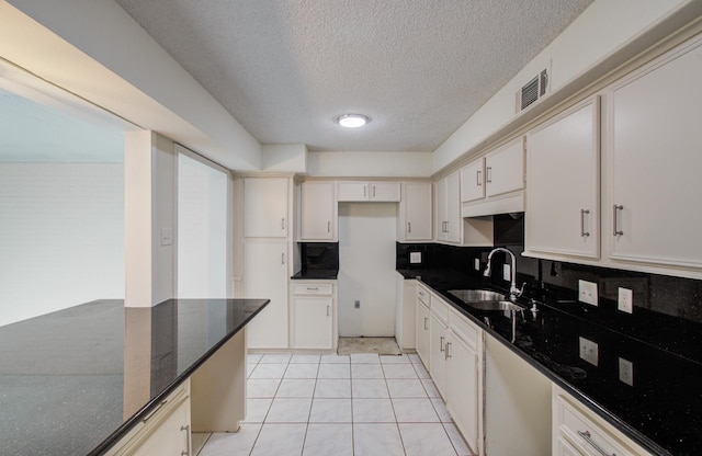 kitchen with visible vents, dark stone counters, light tile patterned flooring, a sink, and tasteful backsplash