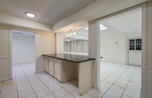 kitchen with a notable chandelier, a textured ceiling, dark countertops, light tile patterned flooring, and brick wall