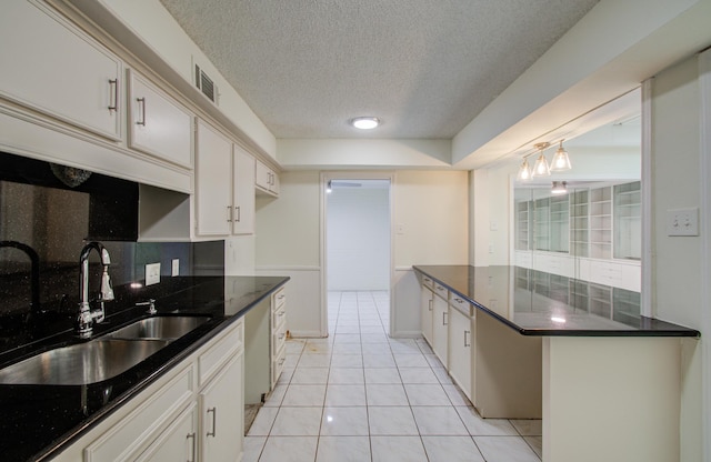 kitchen featuring a textured ceiling, white cabinets, light tile patterned floors, and a sink