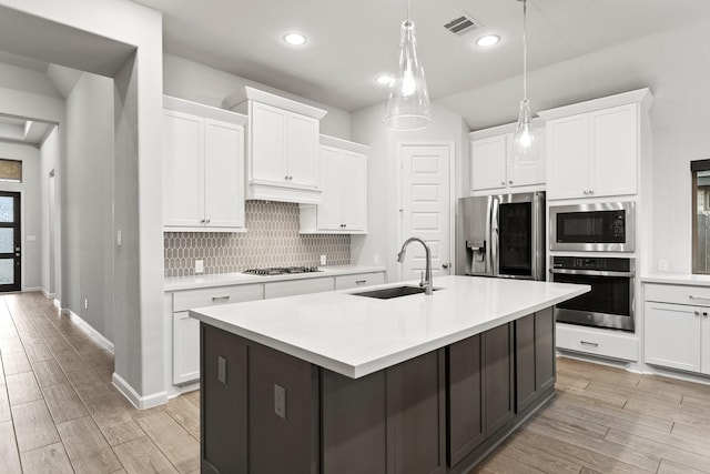 kitchen featuring wood tiled floor, a sink, decorative backsplash, light countertops, and appliances with stainless steel finishes