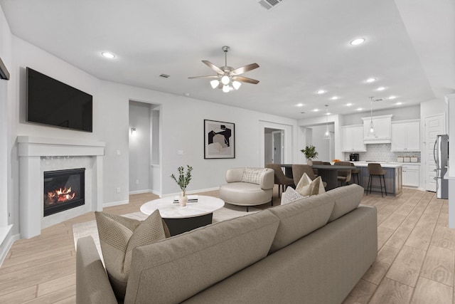 living area featuring visible vents, a glass covered fireplace, recessed lighting, light wood-style floors, and ceiling fan