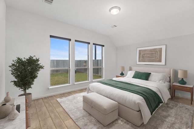 bedroom with visible vents, lofted ceiling, baseboards, and wood finished floors