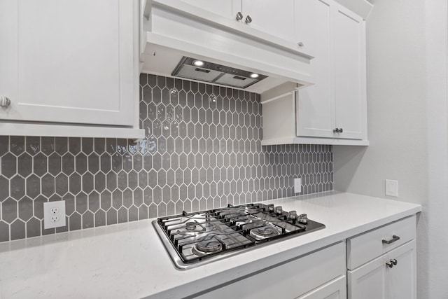 kitchen with under cabinet range hood, backsplash, stainless steel gas stovetop, and white cabinetry
