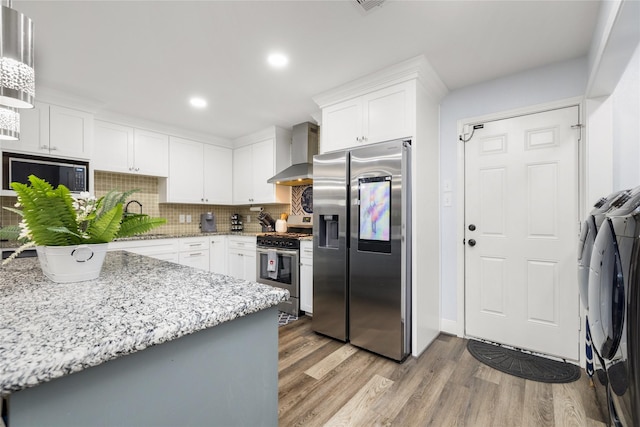 10618 Donegal Way, Houston, TX 77047 - kitchen with washing machine and clothes dryer, appliances with stainless steel finishes, wall chimney range hood, a sink, and light wood-style floors