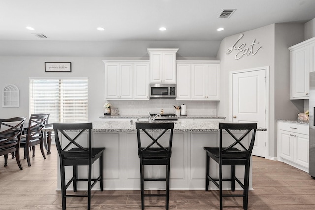 156 Buckeye Dr, Montgomery, TX 77316 - kitchen featuring white cabinetry, stainless steel microwave, backsplash, visible vents, and a center island with sink