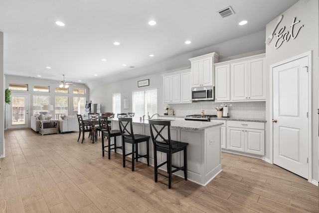 156 Buckeye Dr, Montgomery, TX 77316 - kitchen with ceiling fan, light wood finished floors, a kitchen island with sink, stainless steel microwave, and visible vents