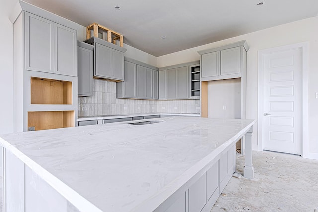 197 Peninsula Point Dr, Montgomery, TX 77356 - kitchen featuring gray cabinets, a spacious island, tasteful backsplash, light stone counters, and concrete flooring