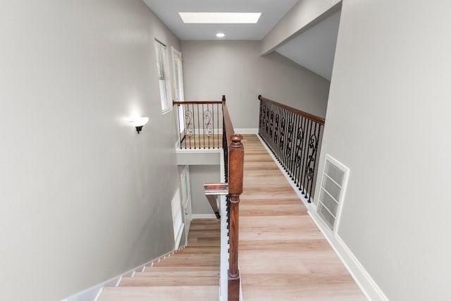stairway with wood finished floors, visible vents, baseboards, a skylight, and beamed ceiling