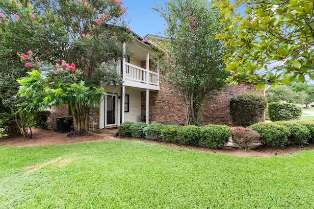view of property hidden behind natural elements featuring a front lawn and a balcony