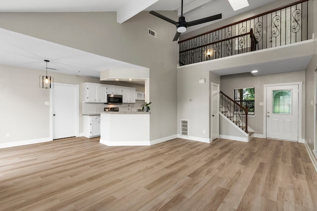 unfurnished living room with visible vents, beam ceiling, a ceiling fan, stairway, and light wood-style floors
