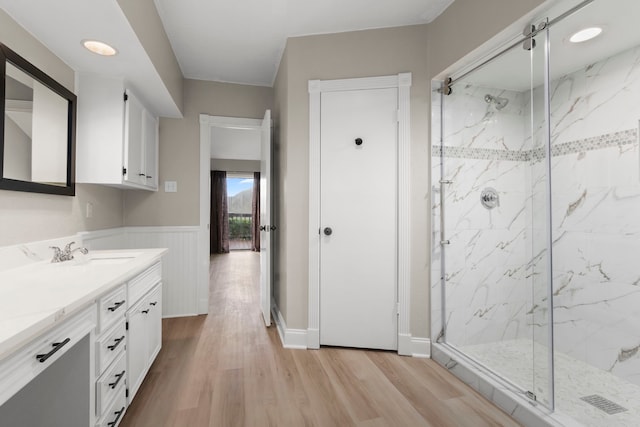 bathroom featuring a marble finish shower, a wainscoted wall, wood finished floors, and vanity