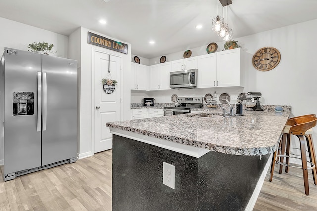 kitchen featuring appliances with stainless steel finishes, white cabinetry, light wood-style floors, and a peninsula