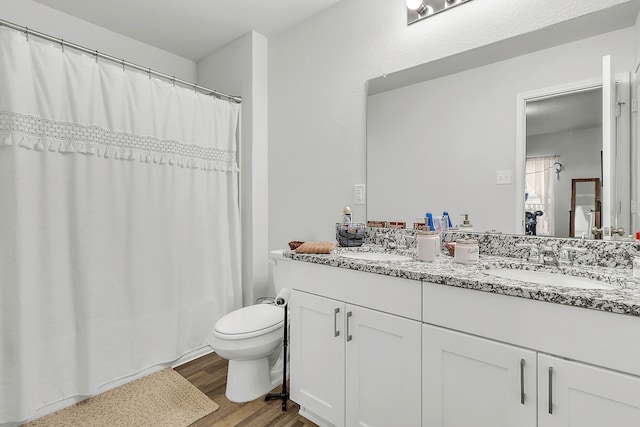full bathroom with double vanity, toilet, wood finished floors, and a sink