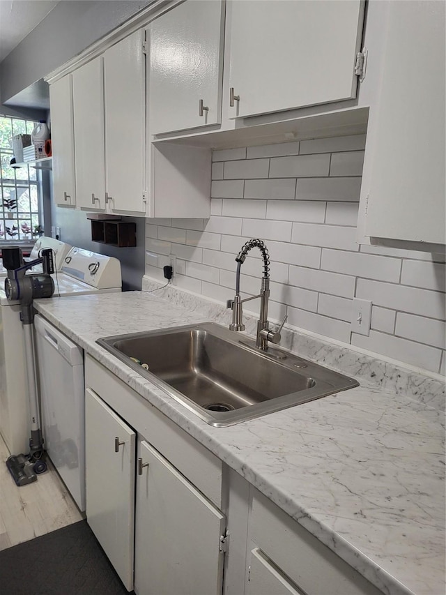 kitchen with tasteful backsplash, light countertops, white dishwasher, white cabinets, and a sink