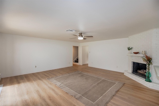 unfurnished living room featuring a ceiling fan, stairs, wood finished floors, a brick fireplace, and visible vents