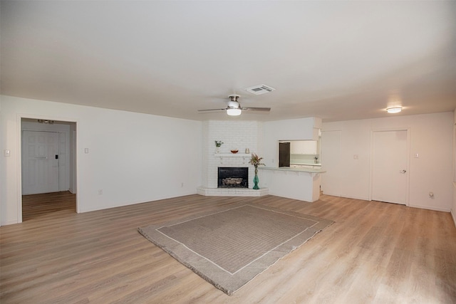 unfurnished living room featuring light wood finished floors, a ceiling fan, visible vents, and a fireplace