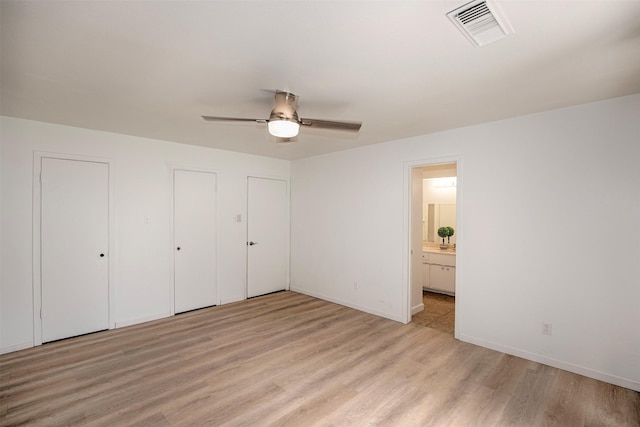 unfurnished bedroom with light wood finished floors, visible vents, connected bathroom, baseboards, and two closets