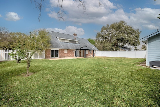 back of house with a lawn, brick siding, a chimney, and a fenced backyard