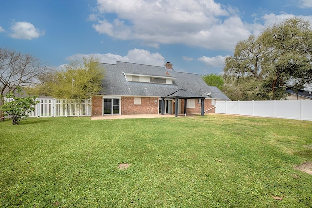 rear view of house featuring a chimney, a fenced backyard, a yard, a patio, and brick siding