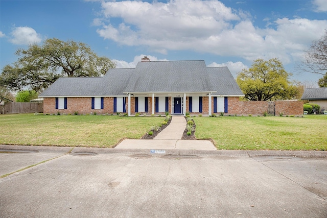 ranch-style house with a front lawn, a chimney, covered porch, fence, and brick siding