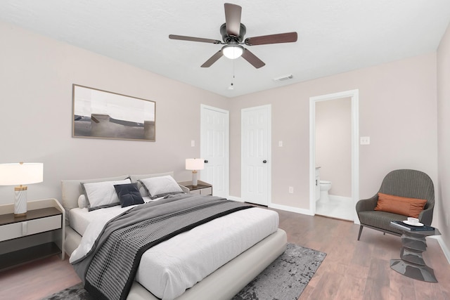 bedroom with visible vents, wood finished floors, baseboards, ensuite bathroom, and a ceiling fan