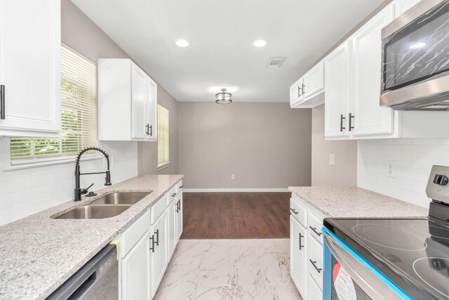 kitchen with white cabinets, light stone countertops, a sink, stainless steel appliances, and backsplash